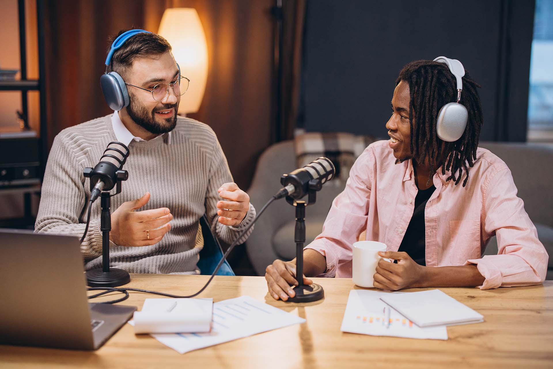 Two podcasters speaking into microphones, wearing headphones during audio recording session
